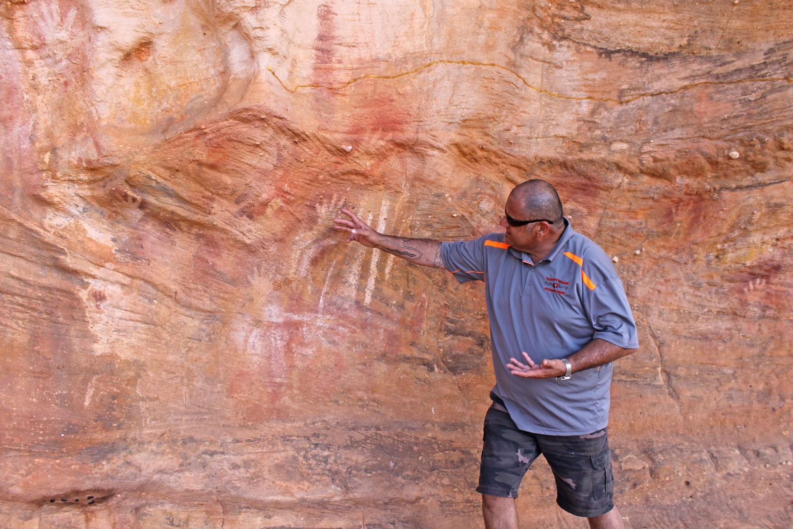 A guide pointing out rock art on a red rock wall at Mutawintji