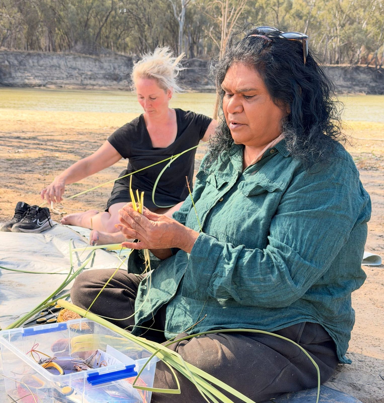 Two women weaving with native grasses on the sand at the eco cultural retreat