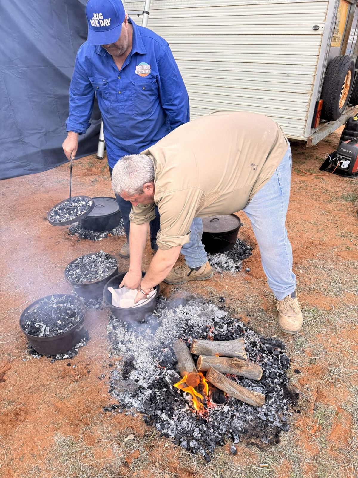 A guide tending a camp oven on hot coals