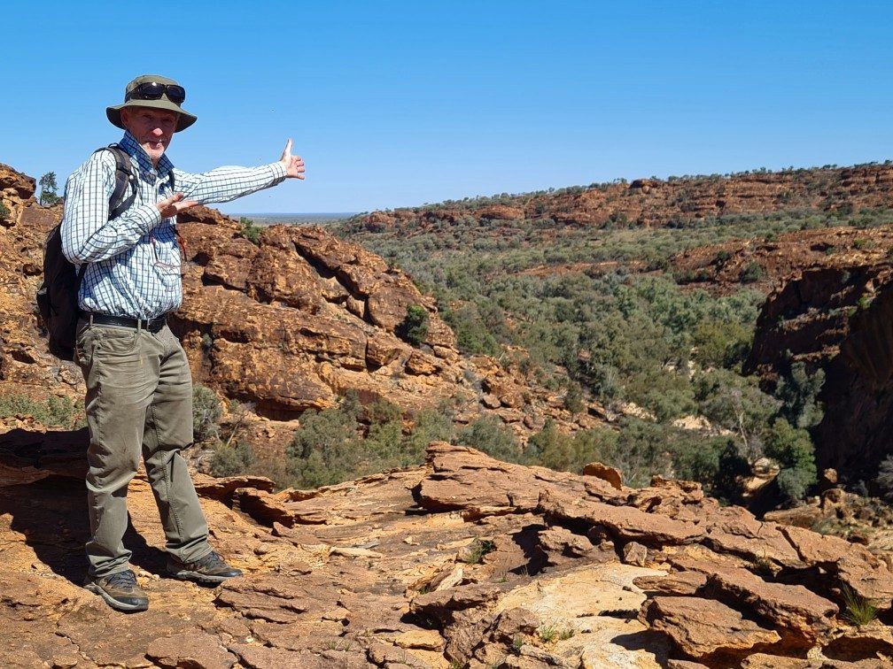 A guide with his arm outstretched on red rocks above a gorge at Mutawintji
