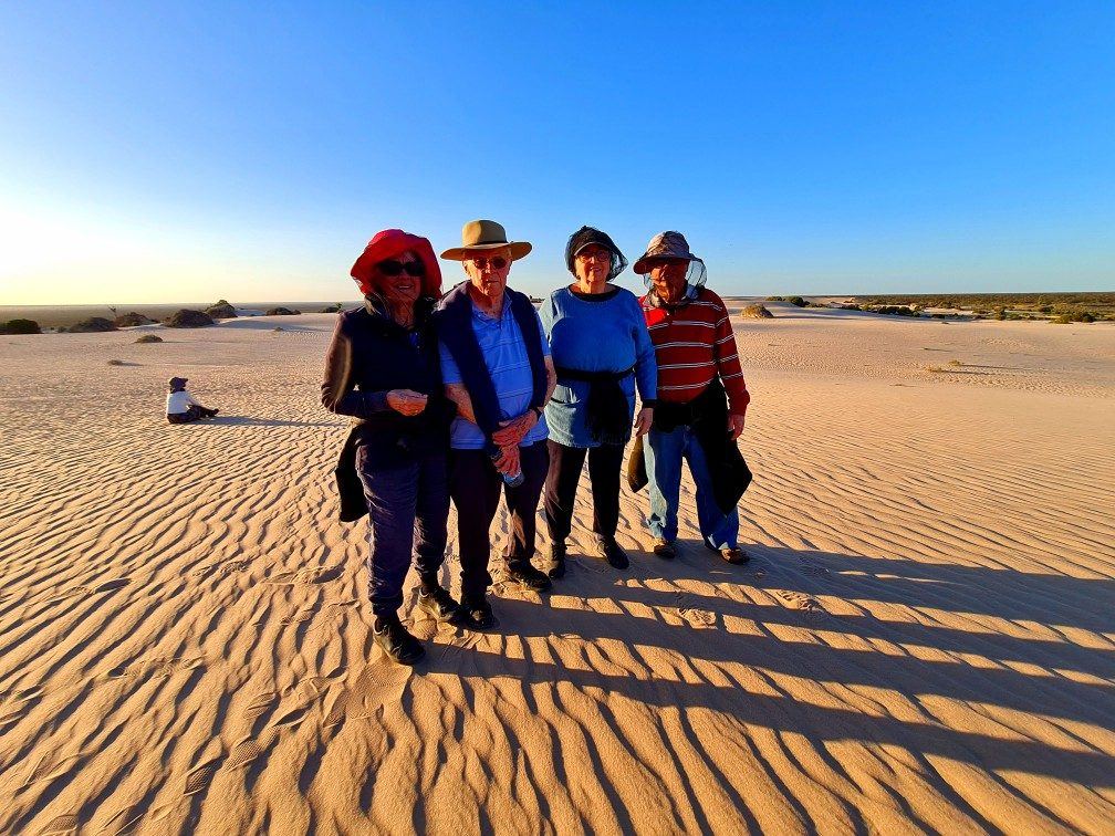 Four guests in hats on rippled red sand dunes at Mungo