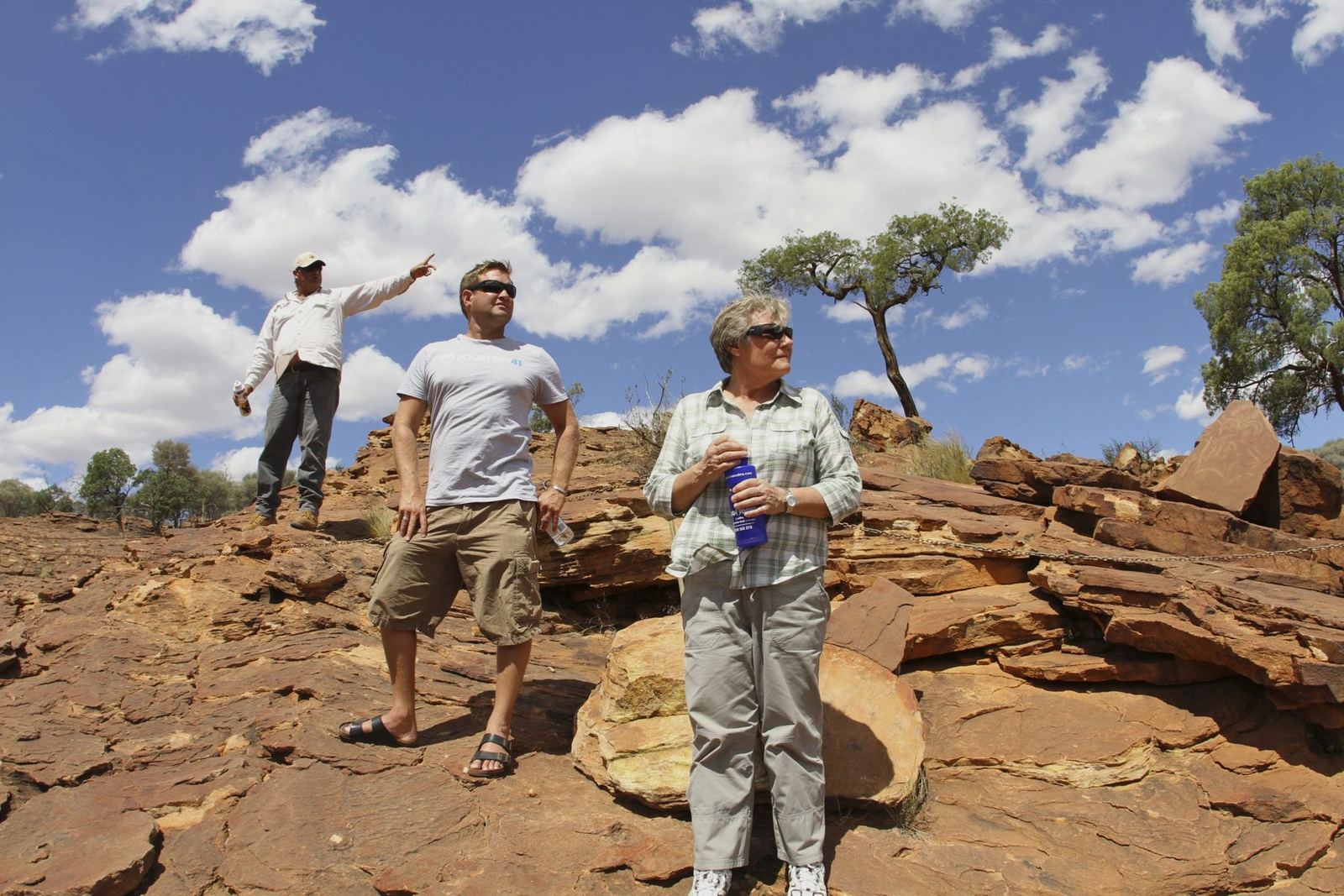 A small group with a guide on red rocks at Mutawintji under a cloudy blue sky