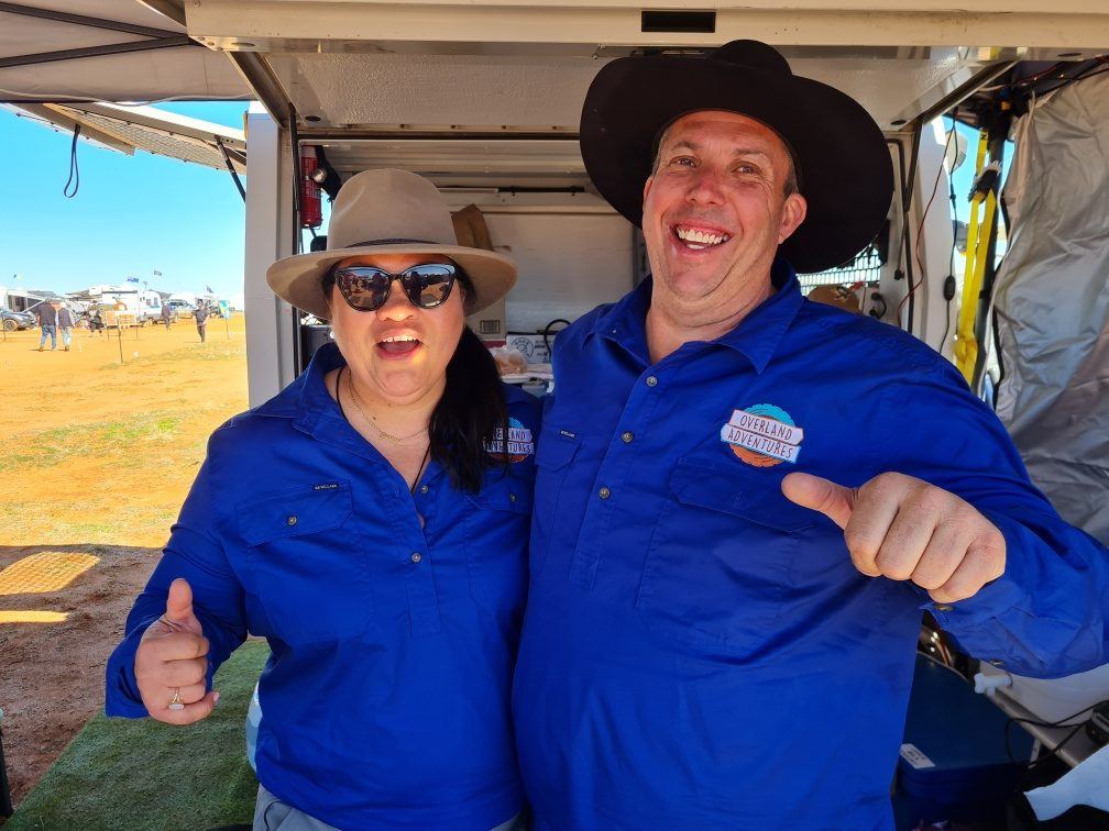 Two smiling Tristate Tours team members giving a thumbs up beside the Overland truck